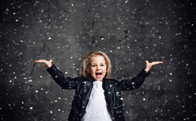 Fototapeta na wymiar Happy screaming kid girl is posing with her hands up spread with open palms under the snow with free copy space above