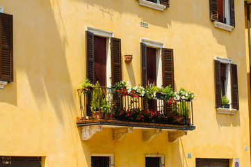 Italian colorful windows with open wooden shutters and fresh flowers. Beautiful european porch decorated with flowers in Italy. Brick wall of an old historical town in Padova, Italy.