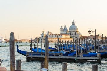 Gold sunset with gondolas docked in Grand Canal, Venice, Italy. Bright sunny panorama view of Grand Canal with gondola and church. Beautiful photo background of the venetian canal in the morning.