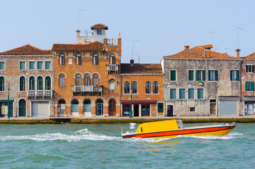 Fototapeta na wymiar Yellow boat in Grand Canal, Venice, Italy. Bright sunny panorama view of Grand Canal with old brick buildings. Beautiful photo background of the venetian canal.