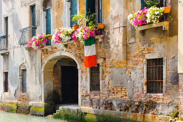 Italian colorful wall with open wooden shutters and fresh flowers. Beautiful european porch decorated with flowers in Italy. Brick wall of an old historical town in Venice, Italy.