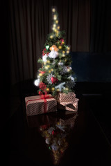 Beautiful small decorated Christmas Tree and many gifts at home with a darkened background