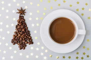 Hot cup of espresso coffee on a table, on a gray background with golden stars, next to a Christmas tree made of coffee beans. Christmas and New Year concept. Top view. Copy space