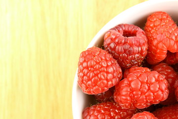 fresh red raspberry fruits in a small white bowl