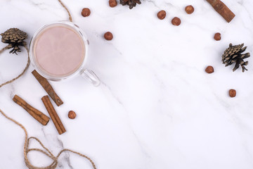 drink cocoa in a glass cup surrounded by winter things wiyh cinnamon on a white table. The concept of cosy holidays