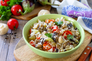 Vegetarian menu, healthy diet food. Rice with vegetables, mushrooms and eggplants in a bowl on a wooden table.