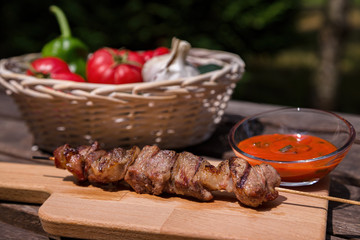 Outdoors summer barbecue, Grilled kebab with vegetables and red sauce on wooden table in the village. Selective focus.