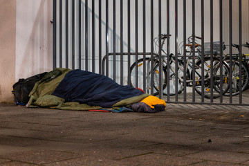 Homeless man sleeping in winter, homeless man in sleeping bag on the street, sidewalk