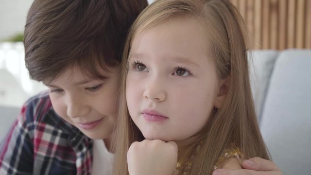 Close-up of Caucasian boy stroking friend's head and hugging cute upset girl. Guy taking care of his first love. Friendship, care.