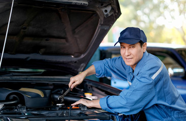 Close up of Asian automotive mechanic with blue uniform check the car in the area of hood and engine in the garage.