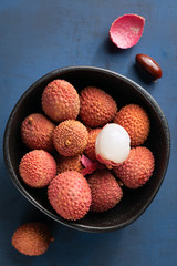 Raw red organic lychee fruit in white bowl on rustic textured concrete background. Copy space.