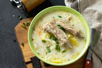 Hot homemade soup with meat ribs and vegetables on a stone countertop.
