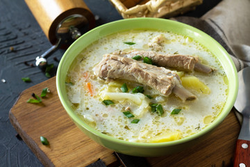 Hot homemade soup with meat ribs and vegetables on a stone countertop.