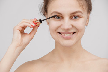 Fototapeta premium Beautiful brunette woman paints the eyelashes. Beautiful woman face. Makeup detail. Beauty girl with perfect skin