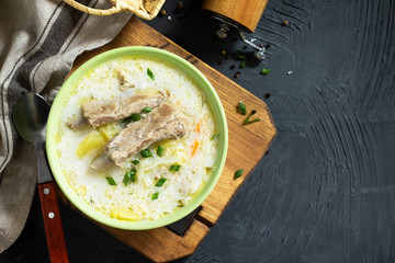 Hot homemade soup with meat ribs and vegetables on a stone countertop. Top view on a flat background lay. Copy space.