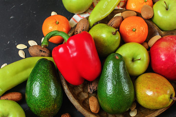 Mixed fruits and vegetables - red peppers, avocado, apples, pears, tangerines, pecan nuts, almonds and pumpkin seeds on wooden bowl, close up view from above