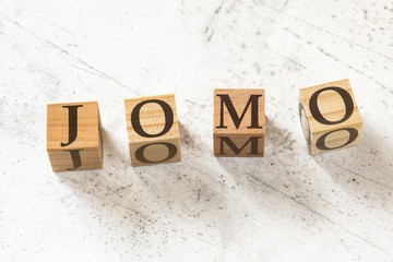 Four wooden cubes with letters JOMO (meaning Joy of missing out) on white working board.