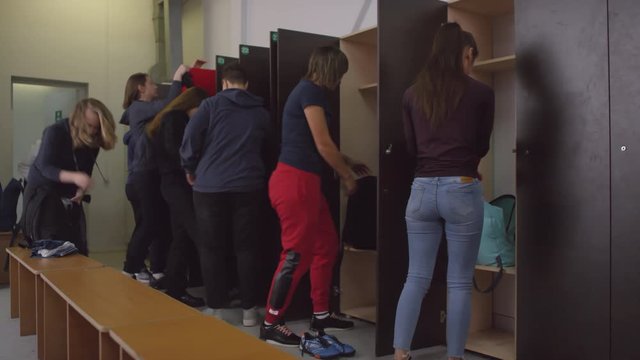 Group of young female soccer athletes changing their clothes, talking and using smartphone in locker room before match