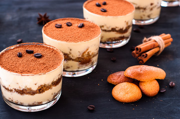 classical tiramisu dessert in a glass sprinkled with cocoa and decorated with coffee beans on a dark background, luxury dessert