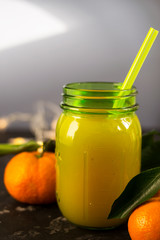 Freshly squeezed orange juice in a mason jar and fresh oranges fruit with green wet leaves on a black shabby background.