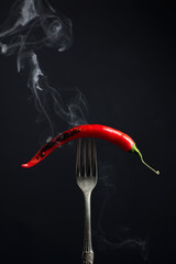 Hot chili red pepper smoking on a fork. Spice concept.