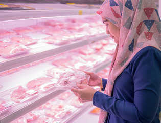 Selective focus Asian adult woman choosing chicken slice in packet at ice aisle inside supermarket.
