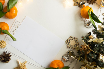 White sheet, postcard lies on the table. Around the layout of citrus fruits, snowflakes, garlands and lights. The concept of a holiday and celebration.