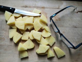 Potato cut into slices or pieces on cutting board along with cook's knife and glasses. Conceptual photo of traditional everyday food cooking process.