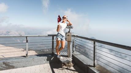 Young woman tourist stands on a viewing platform of Tahtali Mountain in Kemer with a red Turkey flag, Turkey