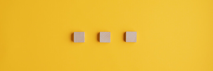 Three blank wooden blocks placed on yellow background