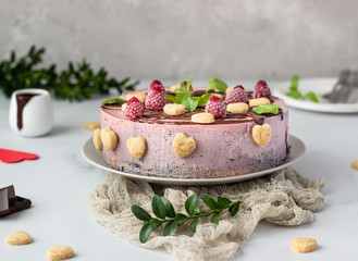No bake raspberry cheesecake (cream mousse dessert) decorated with chocolate glaze, raspberries, heart shape cookies and mint. Valentine’s day concept. Selective focus.