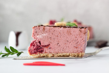 Sliced no bake raspberry cheesecake (cream mousse dessert) decorated with chocolate glaze, raspberries, heart shape cookies and mint. Valentine’s day concept. Selective focus.