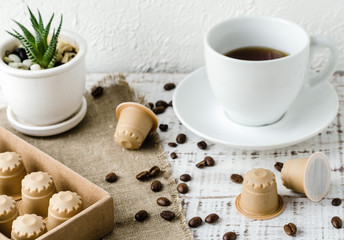 Coffee capsules made from wood. Wooden espresso coffee Capsules, white cup of coffe, coffee beans and flower in a pot on whie wooden table. Zero waste and no plastic concept