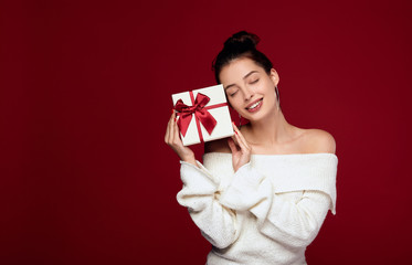 A beautiful lady with bare shoulders holds a gift and smiles with joy.