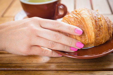 Caucasian woman hand touching buttery croissant in cafe on wooden table background