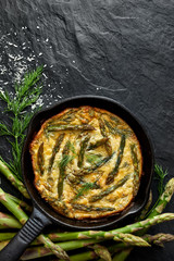 Frittata with green asparagus and fresh dill in in a cast iron skillet on a black background, top view, copy space - obrazy, fototapety, plakaty