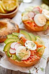 Bagel sandwich with smoked salmon,  avocado, boiled eggs, radish, lemon and fresh dill, close-up. Delicious and healthy breakfast, appetizer