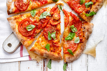 Homemade vegetarian  pizza with addition of tomatoes, mozzarella cheese and basil on a white wooden board, top view. Traditional pizza margherita 