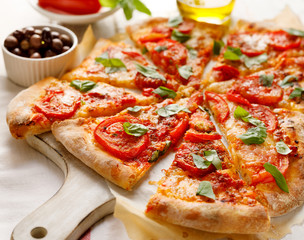 Homemade vegetarian  pizza with addition of tomatoes, mozzarella cheese and basil on a white wooden board, close-up. Traditional pizza margherita