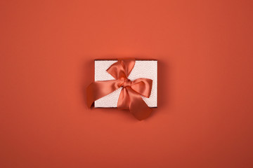 Gift box on a red background. Satin burgundy ribbon bow, box wrapped in craft paper. Luxury gift,...