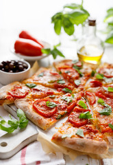 Homemade vegetarian  pizza with addition of tomatoes, mozzarella cheese and basil on a white wooden board, close-up. Traditional pizza margherita 
