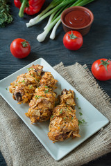 Crispy fried chicken legs breaded with chips. Baked drumsticks are decorated with vegetables and herbs. Fast food. Wrong food. Dark wooden background.