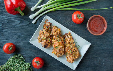 Crispy fried chicken legs breaded with chips. Baked drumsticks are decorated with vegetables and herbs. Fast food. Wrong food. Dark wooden background.