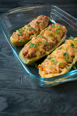Stuffed zucchini with minced meat and grated cheese in a glass baking sheet. Dark wooden background.Healthy balance food.Cooking food.