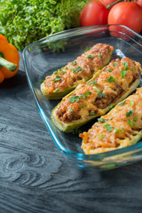 Stuffed zucchini with minced meat and grated cheese in a glass baking sheet. Dark wooden background.Healthy balance food.Cooking food.
