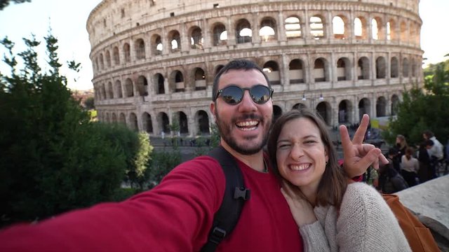 Happy young tourist couple making selfie in front of colosseum in rome, italy. Beautiful smiling people in honeymoon traveling in the capital of Italy. Slow motion video