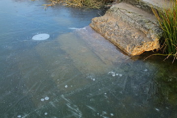 Stairs to the lake frozen in ice. Transparent ice on the lake in winter. The bottom of the lake is visible through the ice. It's dangerous to walk on thin ice