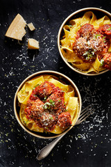 Meat balls in tomato sauce with pappardelle pasta sprinkled with parmesan cheese and fresh basil in a bowl on a black background top view