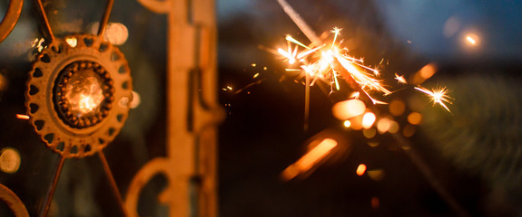 Sparkler for Christmas on the background of a beautiful lamp and in the New Year's surroundings, the atmosphere of the holiday and the weekend, photo in form of banner