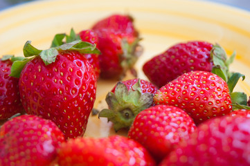 Red berries of garden strawberries with green sepals on a sunny yellow porcelain plate.